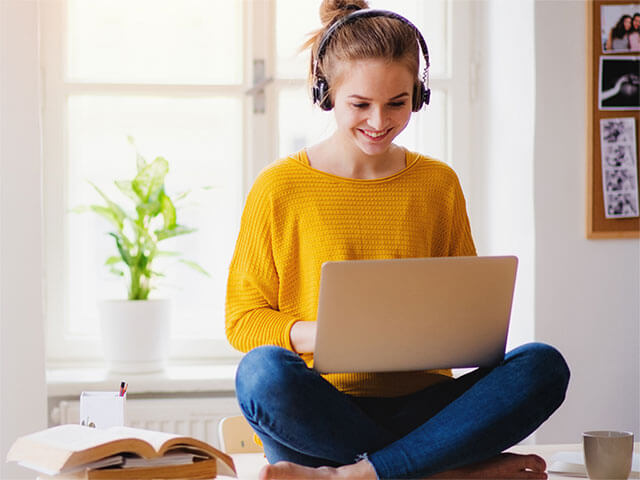 A women wearing headphones and looking at a laptop