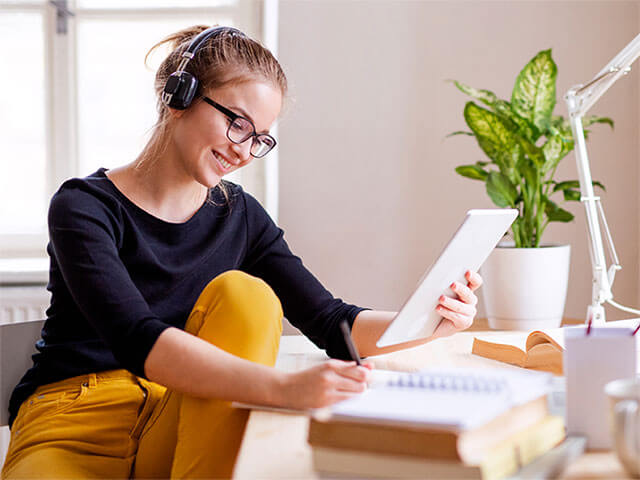 A lady holding a tablet in one hand and writing notes with the other