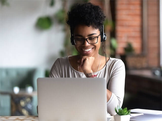 A lady sat at a desk wearing a headset and looking at a laptop