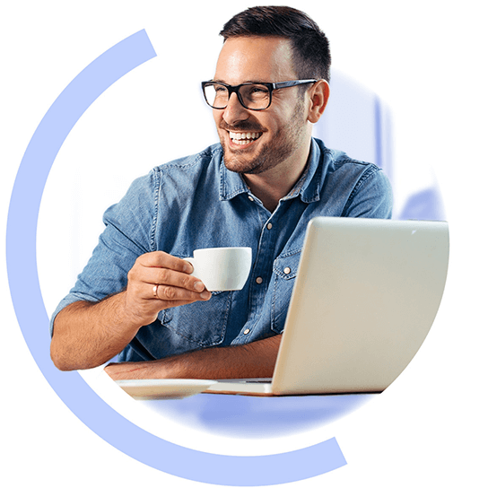 A man sat down at at table with a laptop on it holding a cup